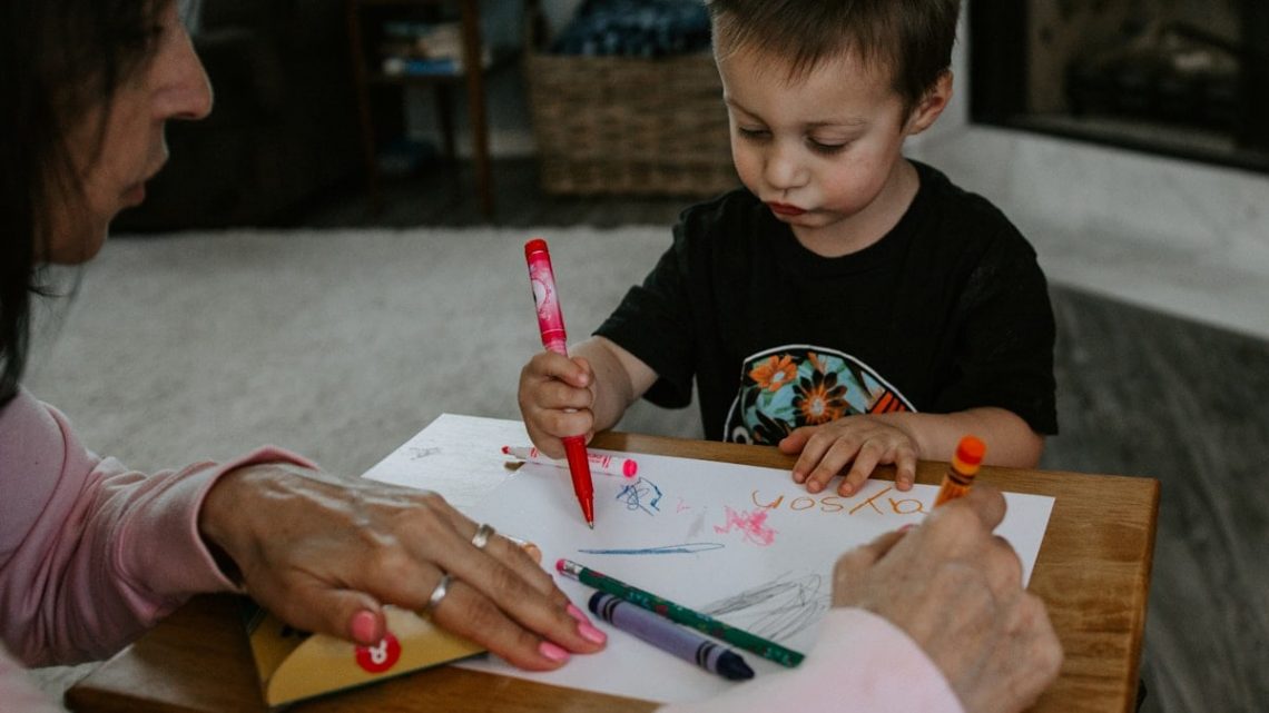 boy in black crew neck t-shirt holding pink pen writing on white paper
