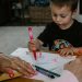 boy in black crew neck t-shirt holding pink pen writing on white paper